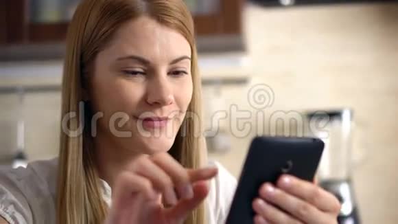 一位漂亮的年轻女子坐在厨房里浏览互联网和微笑视频的预览图