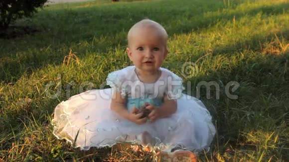一个小女孩穿着白色连衣裙坐在草地上拿着一根冷杉夏天日落视频的预览图