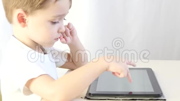 快乐的小男孩坐在桌子旁玩平板电脑特写孩子在玩电子游戏特写镜头这就是视频的预览图