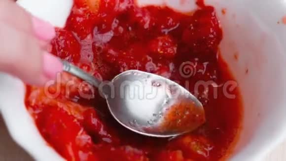 女人用勺子揉草莓把它和糖混在一起做果酱特写的手视频的预览图