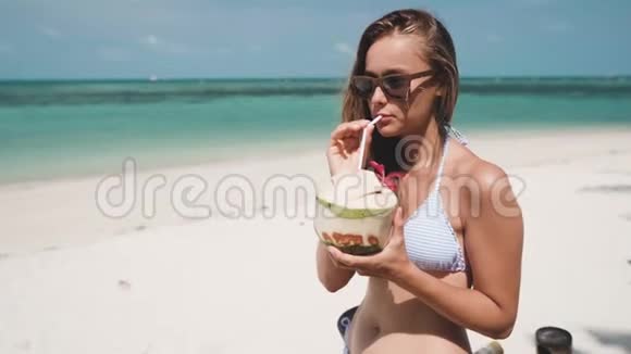女人在沙滩上用稻草喝新鲜的椰子水视频的预览图