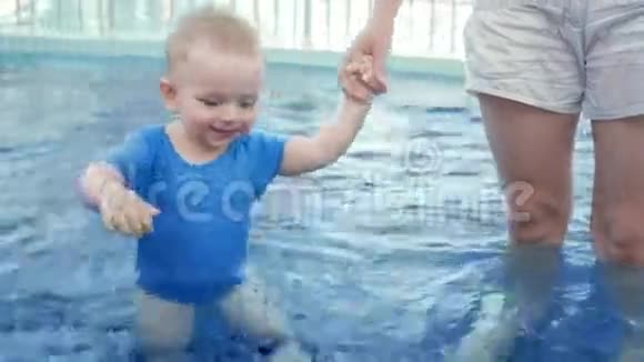 妈妈牵着一个孩子手在街上的游泳池里两岁以下的金发男孩视频的预览图