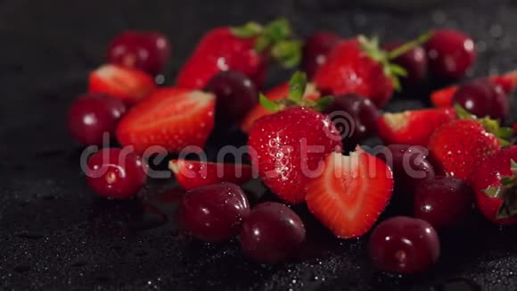 草莓和樱桃在潮湿的黑色表面视频的预览图