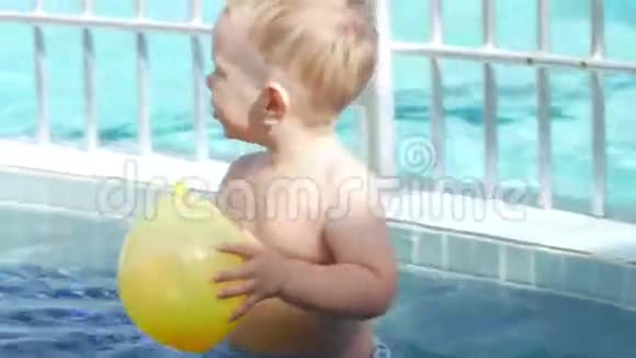 一个可爱的孩子用一个充气黄色球在儿童游泳池里玩耍他用脚走在底部视频的预览图