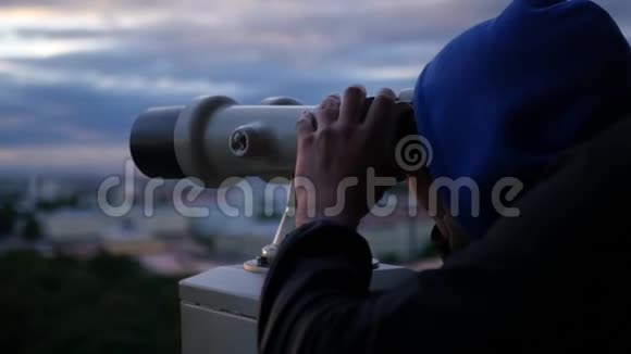 一个年轻人手里拿着望远镜在日落时看城市的全景慢动作1920x1080满的视频的预览图