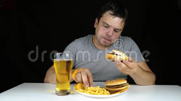 一个贪婪的胖子在黑色背景下吃汉堡的画像视频的预览图