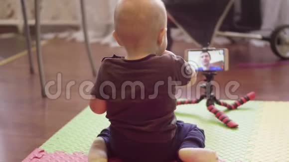 坐在地板上的小孩子在智能手机上与他的白种人爸爸通过视频通话室内4K背部视频的预览图