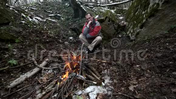 中年人坐在森林里的炉火旁视频的预览图