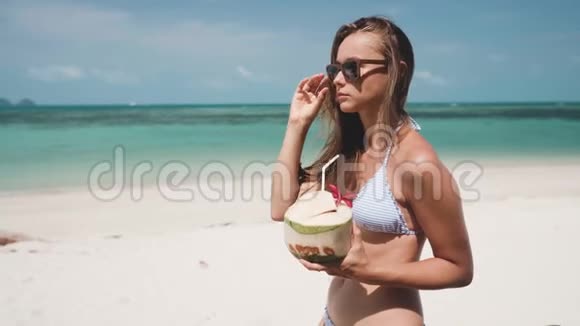 女人在沙滩上用稻草喝新鲜的椰子水视频的预览图