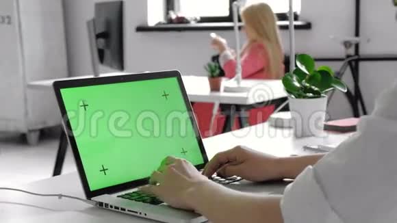 一个人的手在笔记本电脑上绿色屏幕上工作的特写背景模糊明亮的办公室视频的预览图