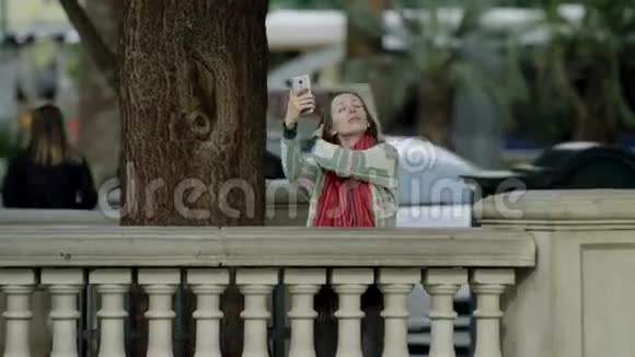 年轻漂亮的女人正在人行道上用智能手机自拍视频的预览图
