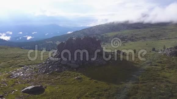 在带有阳光背景的山地草地上的孤独岩石上的戏剧性景色在山顶的巨大岩石上的鸟瞰图视频的预览图