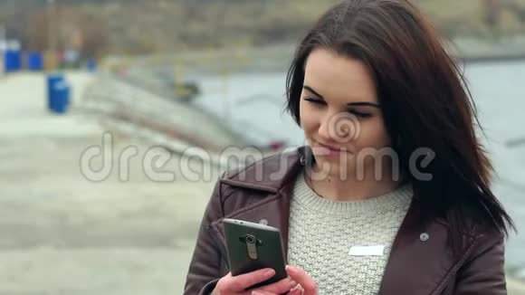 一个棕色长发的年轻漂亮女孩的肖像女孩看着智能手机上的信息多云视频的预览图