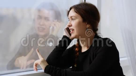 一个年轻的女人在电话上愉快地交谈手指在窗户上画画视频的预览图