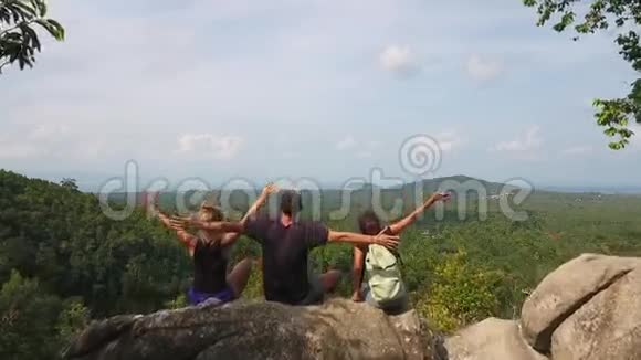 三位无忧无虑的年轻游客坐在岩石上两手散落在一边欣赏大自然的美丽视频的预览图