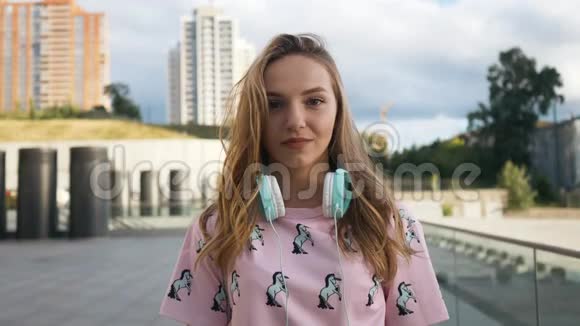 城市带耳机和背包的白人年轻女性魅力可爱的微笑慢动作肖像视频的预览图