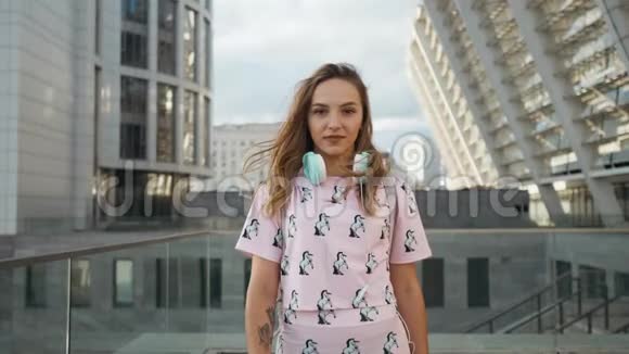 城市带耳机和背包的白人年轻女性魅力可爱的微笑慢动作肖像视频的预览图