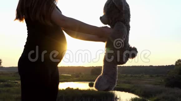 可爱的莫奈年轻的怀孕女孩在日落时和熊玩视频的预览图