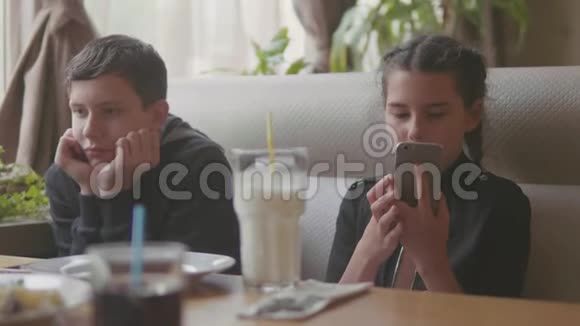 两个可爱的孩子一起室内一起喝奶昔或调味饮料慢动作视频使智能手机处于运行状态视频的预览图