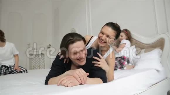 一家人在家里的床上玩耍时不安分活跃有迷人笑容的年轻父母视频的预览图