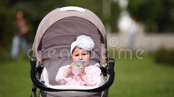 可爱的女婴坐在马车里在公园里喝牛奶视频的预览图