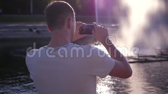 男人在一个美丽的喷泉的电话上拍了一张照片溅了溅和眩光下面的动作高清1920x1080视频的预览图