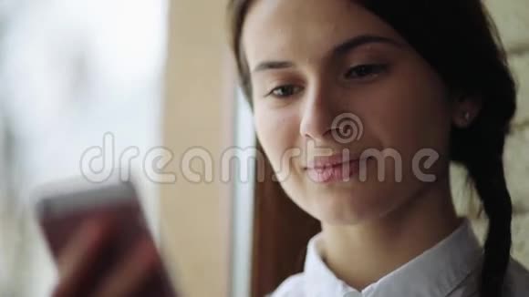美丽的年轻休闲女性使用手机看着她办公室的窗户视频的预览图