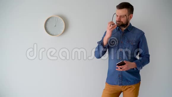 一个长胡子的人用智能手机对着灰色的墙挂着一只钟视频的预览图