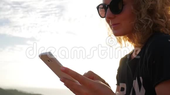 年轻的卷发女人用手机高清慢镜头与美丽的日落镜头耀斑泰国视频的预览图