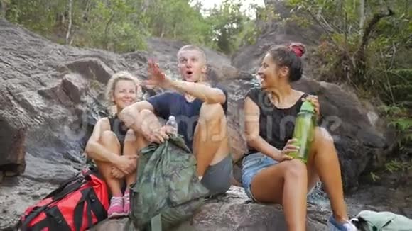 一群年轻的游客笑着休息在瀑布旁高清慢速运动泰国视频的预览图