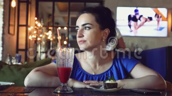 年轻漂亮的黑发女郎穿着带花边的蓝色连衣裙坐在咖啡馆里喝鸡尾酒在电话里写些什么视频的预览图
