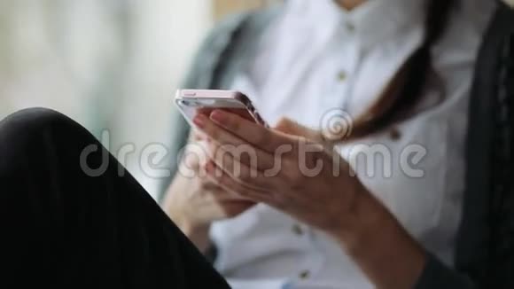 年轻漂亮的女人在现代办公室的智能手机上发短信靠在坐在窗台上的砖墙上视频的预览图