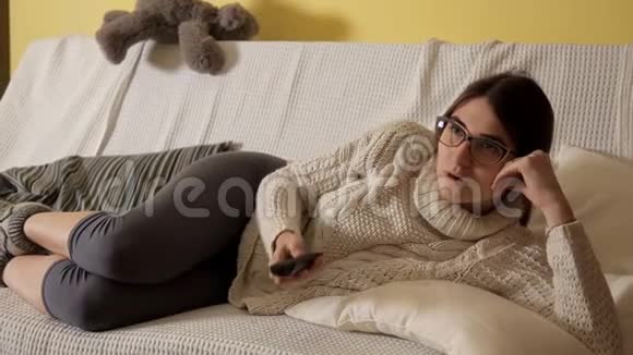冬天晚上小女孩穿着白色毛衣在沙发上看电视戴着眼镜晚上好房子舒适舒适视频的预览图