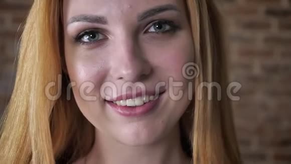 年轻快乐的金发女孩的脸正在镜头前看着微笑着砖色背景视频的预览图