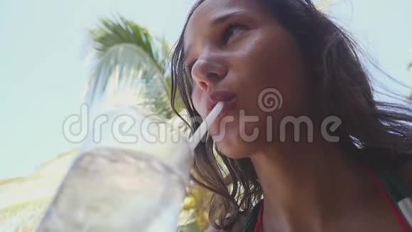 年轻漂亮的女人在棕榈树的背景上喝水从底部看慢动作1920x1080视频的预览图