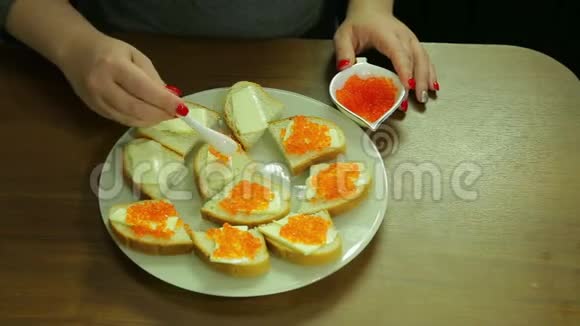 一个女人从一勺鱼子酱中取出红色的鱼子酱用黄油涂在罐头上视频的预览图
