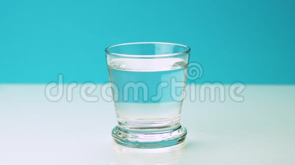 一粒止痛的泡腾药丸落入玻璃杯中将慢镜头的阿司匹林溶解在一片水蓝色的水中视频的预览图