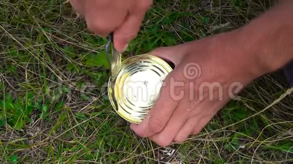 强壮的男人他的手打开一个铁罐用刀子在草地上打鱼在上面拍摄特写视频的预览图