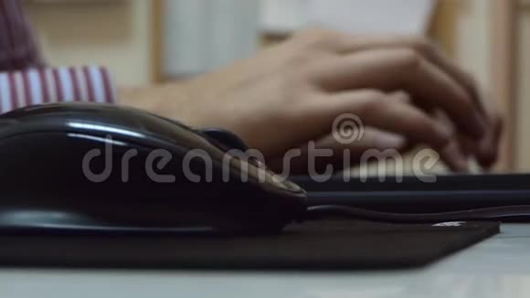 男性手在笔记本电脑上工作在办公室的黑垫上摸黑老鼠视频的预览图