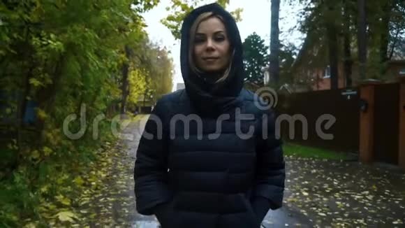 一位身穿黑色夹克衫头罩在秋日小路上行走的肖像女子视频的预览图