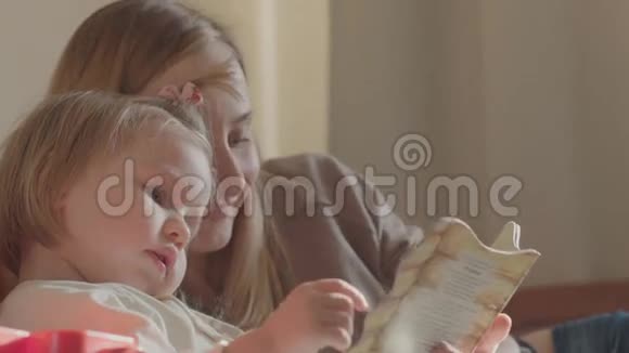 一位微笑的年轻可爱的母女在床上躺着看书放松的画像视频的预览图