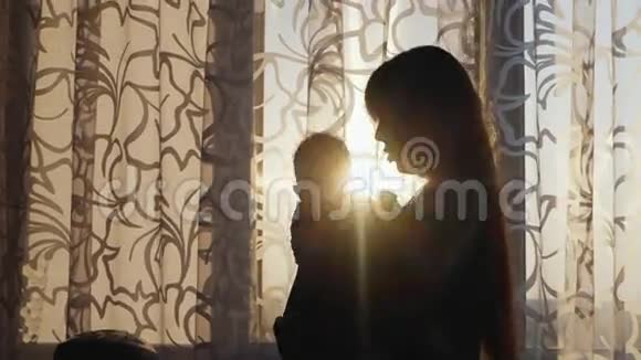 一位年轻母亲的剪影窗前有个孩子把婴儿抱在怀里视频的预览图