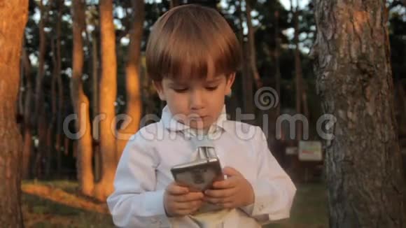 一个穿着黑色马裤的小男孩一件带领带的白色衬衫接电话在智能手机上交谈日落视频的预览图