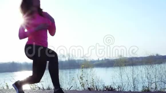 活泼的女孩在日出或日落时沿着河岸慢跑运动女性的健康生活方式观念视频的预览图