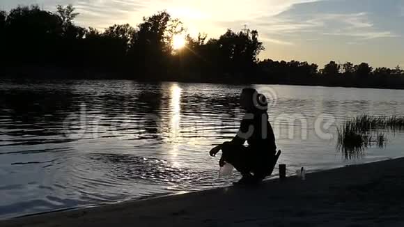 一个年轻的女人坐在湖畔在日落时泼水视频的预览图