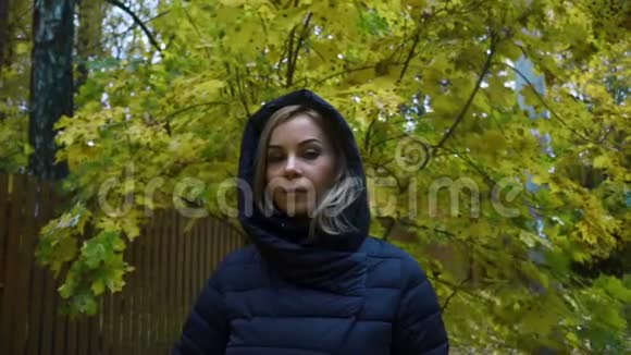 一位身穿黑色夹克头罩在秋天自然背景上的年轻女子的肖像视频的预览图