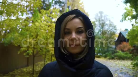 一位身穿黑色夹克衫头罩在秋日小路上行走的肖像女子视频的预览图