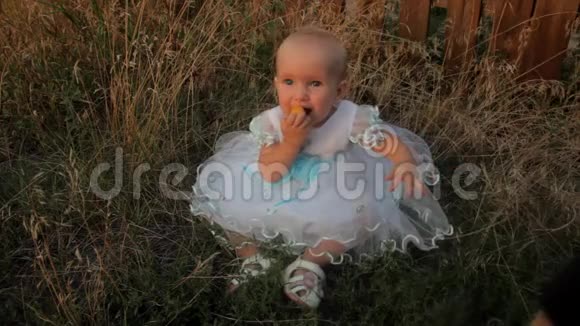 一个小女孩坐在高高的草地上穿着白色的裙子吃着杏子一个小男孩坐在她身边带了她视频的预览图