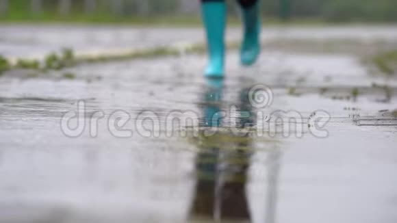 穿着蓝色橡胶靴的女人在水坑上跳跃的特写镜头视频的预览图