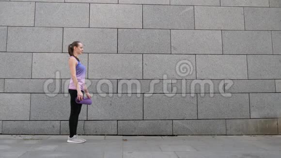 女人在灰色的城市背景上卷起瑜伽垫自由健康和瑜伽理念近距离射击视频的预览图